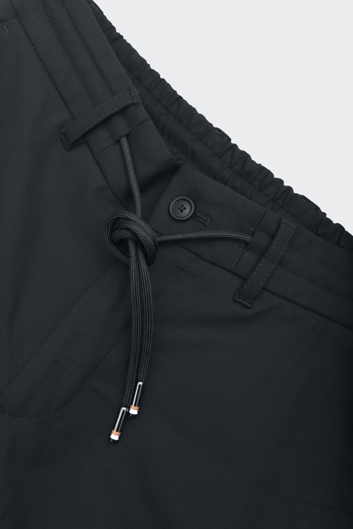 Joggers smart fit color negro con diseño formal, cintura elástica y ajustable, tejido transpirable y resistente, ideales para viajar con estilo y comodidad. Foto detalle botón.